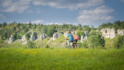 Radfahrer bei den 12 Apostel Solnhofen Zwei Personen fahren mit Fahrrädern auf einem grasbewachsenen Feld vor einer Felslandschaft.